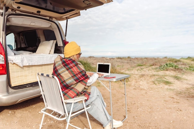 La mujer adulta trabaja en una computadora portátil mientras viaja con una autocaravana Concepto de estilo de vida de la gente moderna en trabajo inteligente o libertad nómada digital