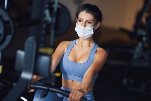 Mujer adulta trabajando en un gimnasio en máscara debido a covid-19