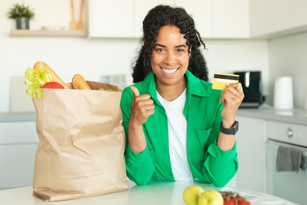 mujer africana, actuación, tarjeta de crédito, posar, con, bolsa, en, cocina