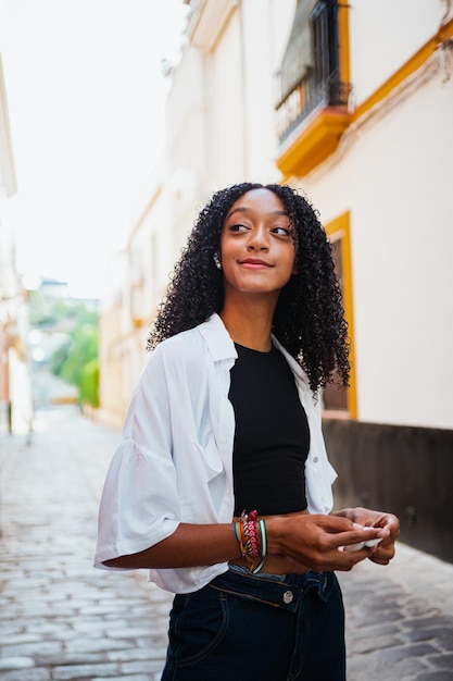 Mujer africana alegre escuchando música en auriculares inalámbricos y sosteniendo el estuche de carga