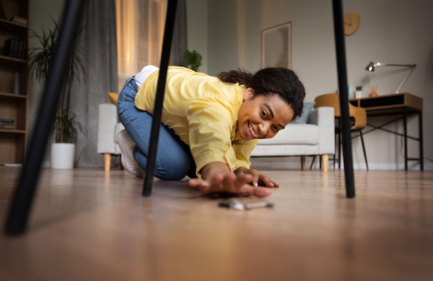 Mujer africana alegre tomando objeto del piso en casa