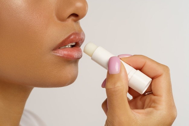 Mujer africana aplicar lápiz labial bálsamo higiénico para labios hidratante y protección contra el frío y el viento