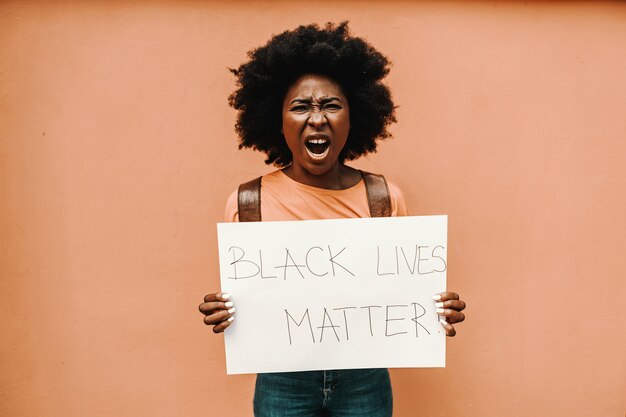 ¡Mujer africana atractiva que sostiene el papel con la MATERIA DE VIDAS NEGRAS! y gritando.