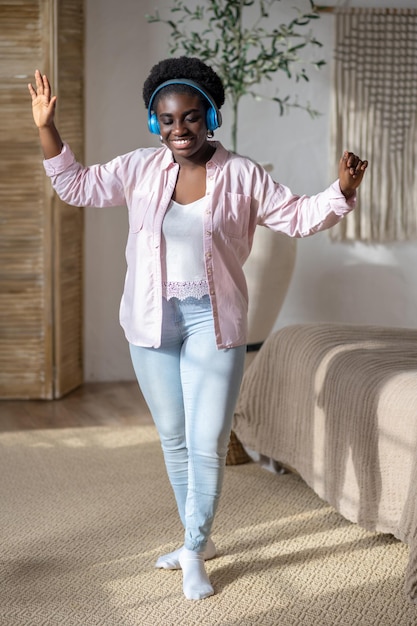 Una mujer africana con auriculares sintiéndose alegre y bailando