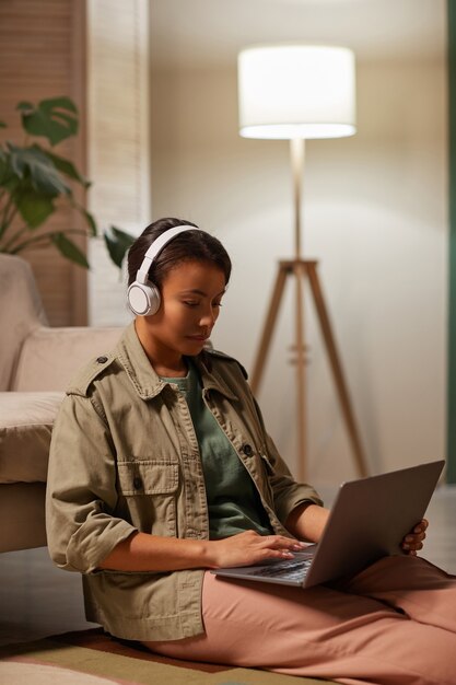 Mujer africana en auriculares trabajando en línea en su computadora portátil sentada en el sofá en casa