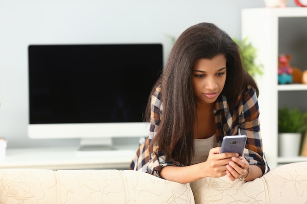 Mujer africana chateando en casa usando un teléfono inteligente