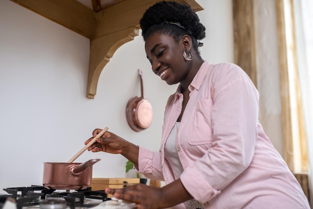 Mujer africana contenta con ropa rosa cocinando en la cocina