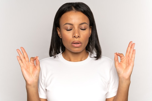 Mujer africana estresada tomados de la mano en gesto de yoga controlar el estrés respirar profundamente con los ojos cerrados