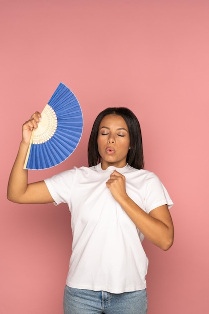 La mujer africana exhausta que usa un ventilador de papel sufre de calor, la sudoración se siente lenta aislada en rosa