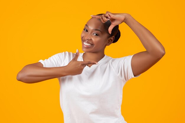 Mujer africana feliz en camiseta blanca hace marco estudio de signos