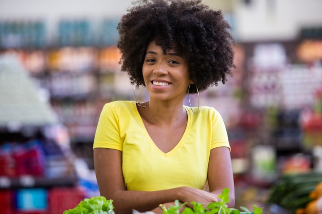 Mujer africana feliz positiva sana sosteniendo un carrito de la compra lleno de frutas y verduras.