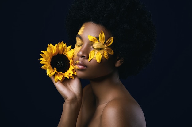 Mujer africana con un girasol y maquillaje creativo en su rostro