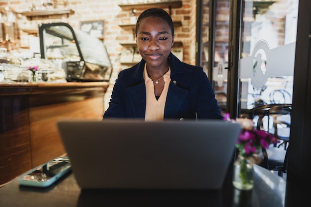 Foto mujer africana haciendo una llamada de video en una computadora portátil mientras está sentada en una cafetería