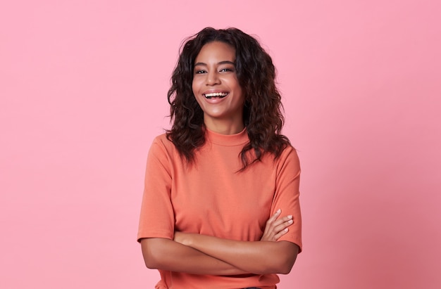 Mujer africana hermosa sonriente feliz que mira la cámara que lleva la camiseta anaranjada casual en rosa.