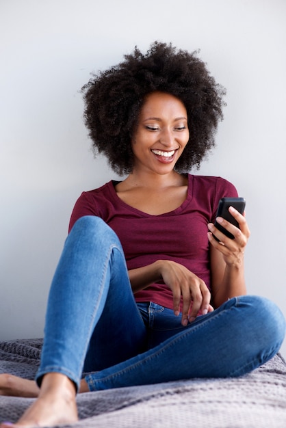 Mujer africana joven feliz que se relaja en casa con el teléfono móvil