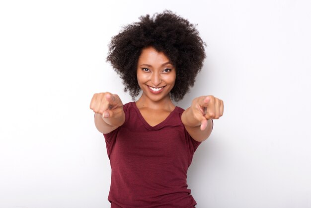 Mujer africana joven feliz que señala ambas manos y que sonríe en el fondo blanco