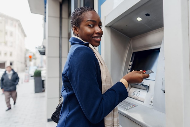 Mujer africana joven que retira efectivo en el cajero automático