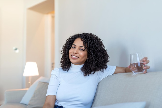 Mujer africana joven en ropa informal bebiendo agua de vidrio