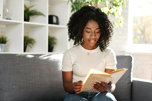 mujer africana, libro de lectura, en casa, sentado, en, sofá