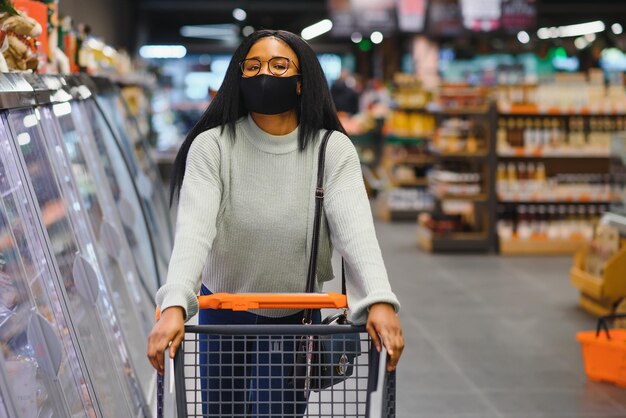Mujer africana con máscara médica desechable comprando en un supermercado durante el brote de pandemia de coronavirus Tiempo epidémico