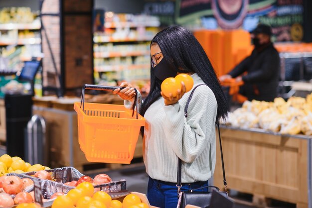 Mujer africana con máscara médica desechable. Compras en el supermercado durante el brote de pandemia de coronavirus. Tiempo de epidemia.