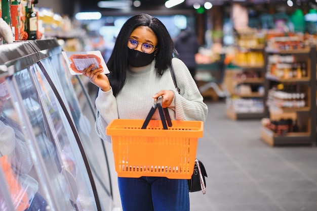 Mujer africana con máscara médica desechable. Compras en el supermercado durante el brote de pandemia de coronavirus. Tiempo de epidemia.