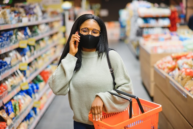 Mujer africana con máscara médica desechable. Compras en el supermercado durante el brote de pandemia de coronavirus. Tiempo de epidemia.