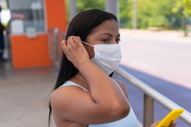 Mujer africana con mascarilla con teléfono en la estación de autobuses.