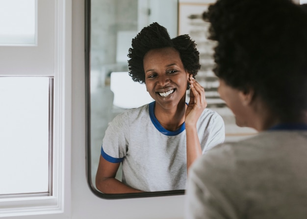 Mujer africana de pie junto al espejo en el baño.