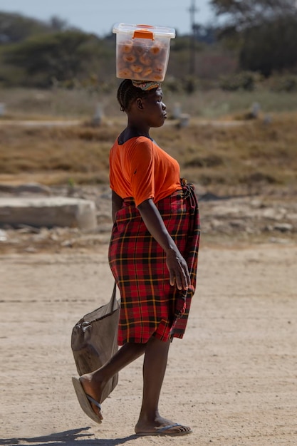 Una mujer africana pobre lleva una caja de comida en la cabeza.