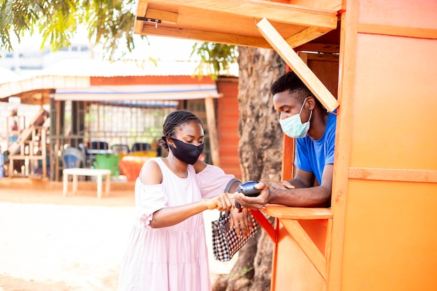 Mujer africana en un quiosco de servicio pos recogiendo algo de dinero para un cliente, usa una máscara facial