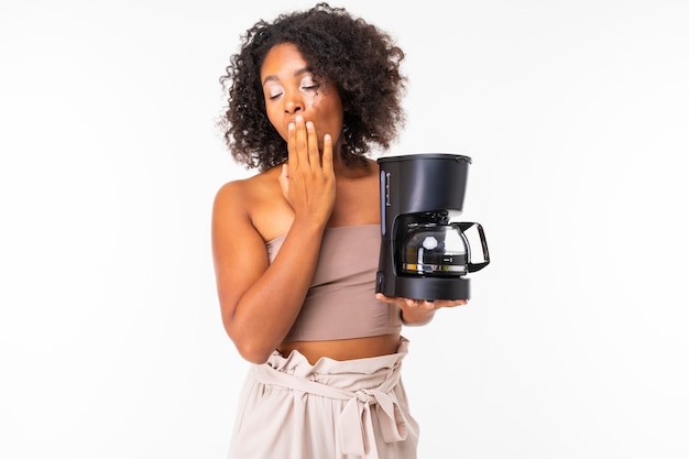 Mujer africana soñolienta en ropa de verano con cafetera, imagen aislada en la pared blanca