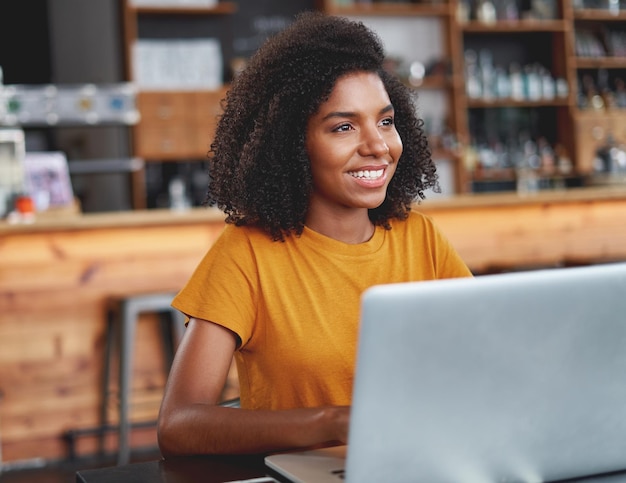 Una mujer africana sonriente con una computadora portátil en un café.