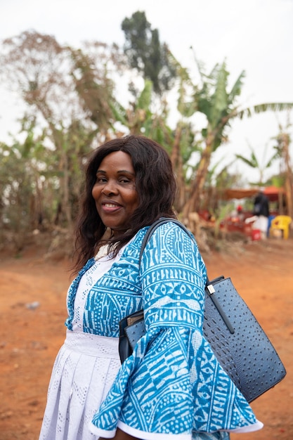 Una mujer africana sonriente vestida con ropa tradicional y llevando una foto vertical de bolsa