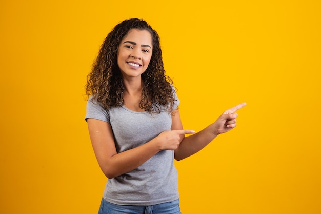 Mujer afro apuntando en fondo amarillo con espacio para el texto