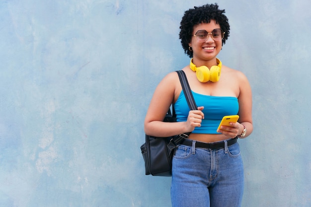 Mujer afro con una blusa azul riendo delante de un fondo azul. Ella esta mirando a la camara