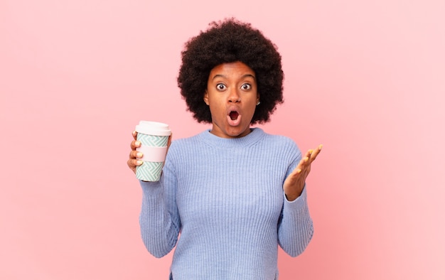 Mujer afro con la boca abierta y asombrada, conmocionada y asombrada con una sorpresa increíble