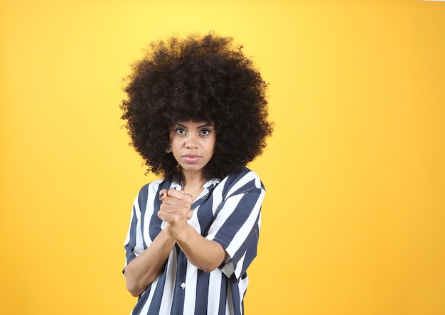 Mujer afro, hace gesto de boxeo, ropa casual, fondo amarillo