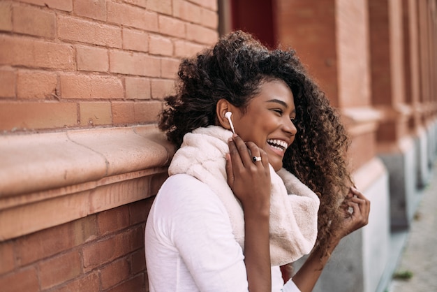Mujer afro hermosa joven al aire libre en música que escucha de la calle de la ciudad con los auriculares.