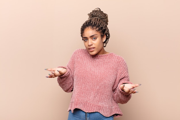 Mujer afro joven que se siente asombrada y con la boca abierta apuntando hacia arriba con sorpresa