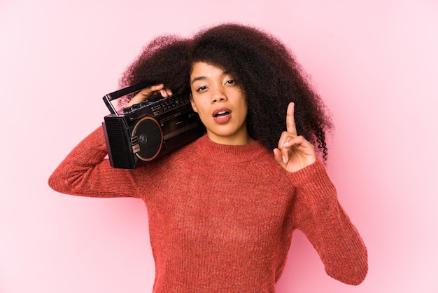 Mujer afro joven que sostiene un cassete aislado teniendo una idea, concepto de la inspiración.