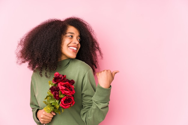 La mujer afro joven que sostiene rosas señala con el dedo pulgar lejos, riendo y despreocupado.