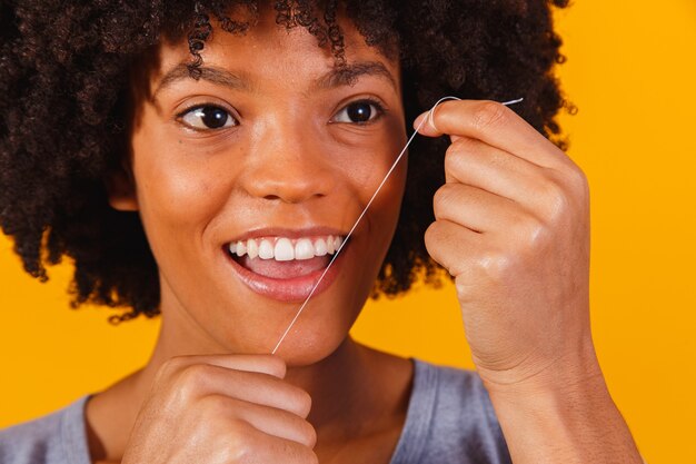 Mujer afro limpiando sus dientes con hilo dental. concepto de salud bucal