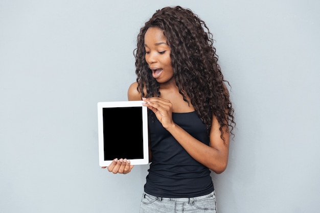 Mujer afro mostrando ordenador portátil en blanco sobre pared gris