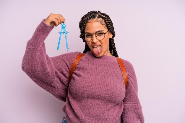 Mujer afro negra con actitud alegre y rebelde, bromeando y sacando la lengua. medir el concepto de estudiante de brújula