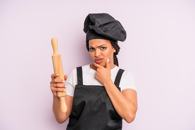 mujer afro negra con la boca y los ojos bien abiertos y la mano en la barbilla. chef con un rodillo