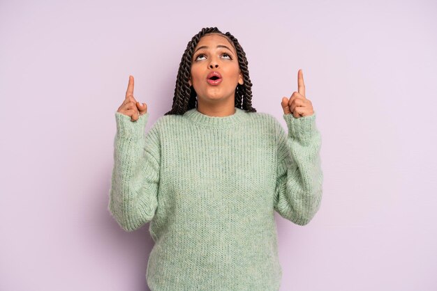 Mujer afro negra que parece sorprendida, asombrada y con la boca abierta, apuntando hacia arriba con ambas manos para copiar el espacio