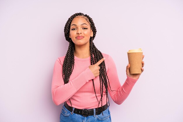 Foto mujer afro negra sonriendo alegremente, sintiéndose feliz y apuntando hacia un lado. café para llevar