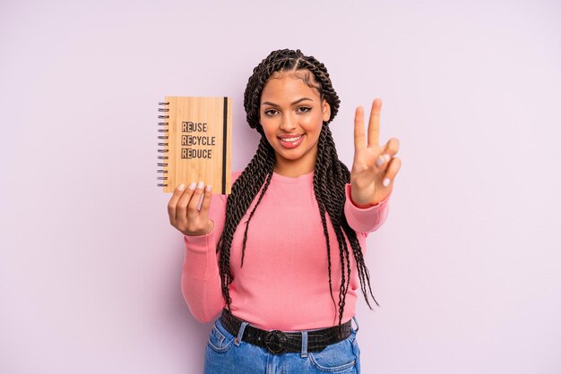 Mujer afro negra sonriendo y luciendo amigable mostrando el concepto de reciclaje número dos