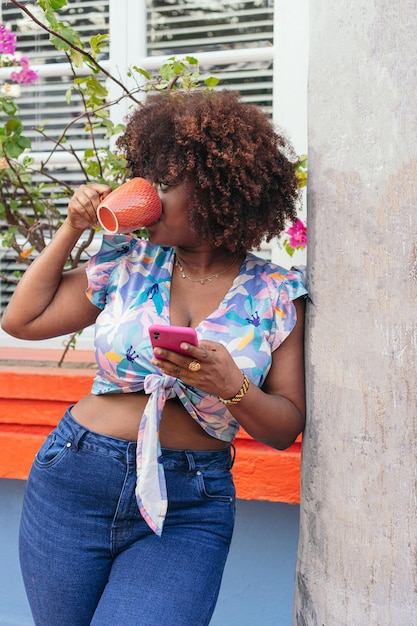 Mujer afro de pie disfrutando de su café en la calle